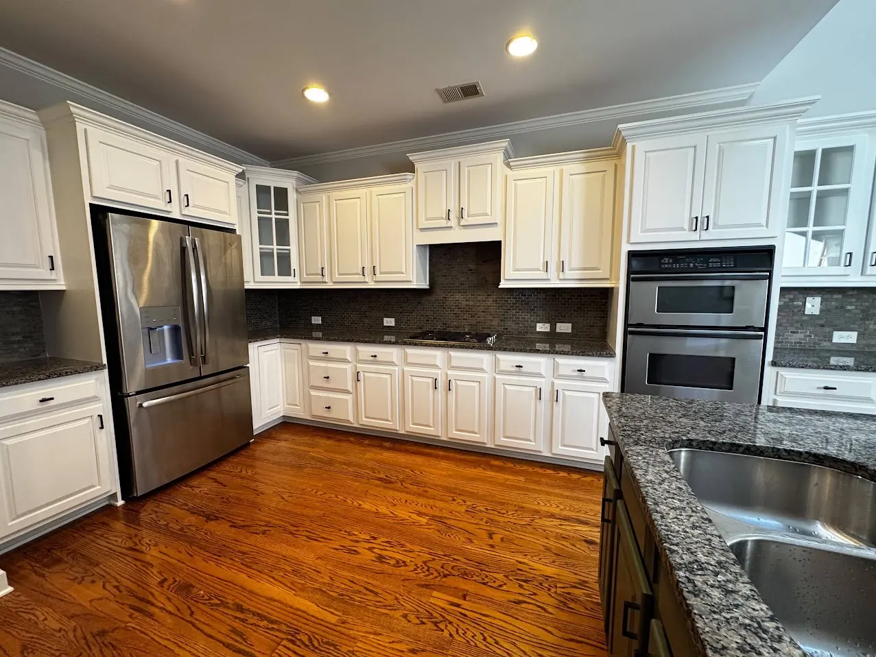 Cabinet Painting Guys client kitchen with white painted cabinets above hardwood floors and built-in ovens